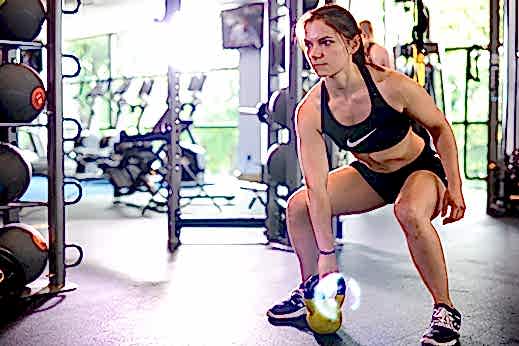 A woman with a determined expression works out with kettle bells in the gym 