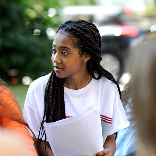 A young women sitting outside in the campus grounds has a pensive expression as she listens to the conversation of her friends 