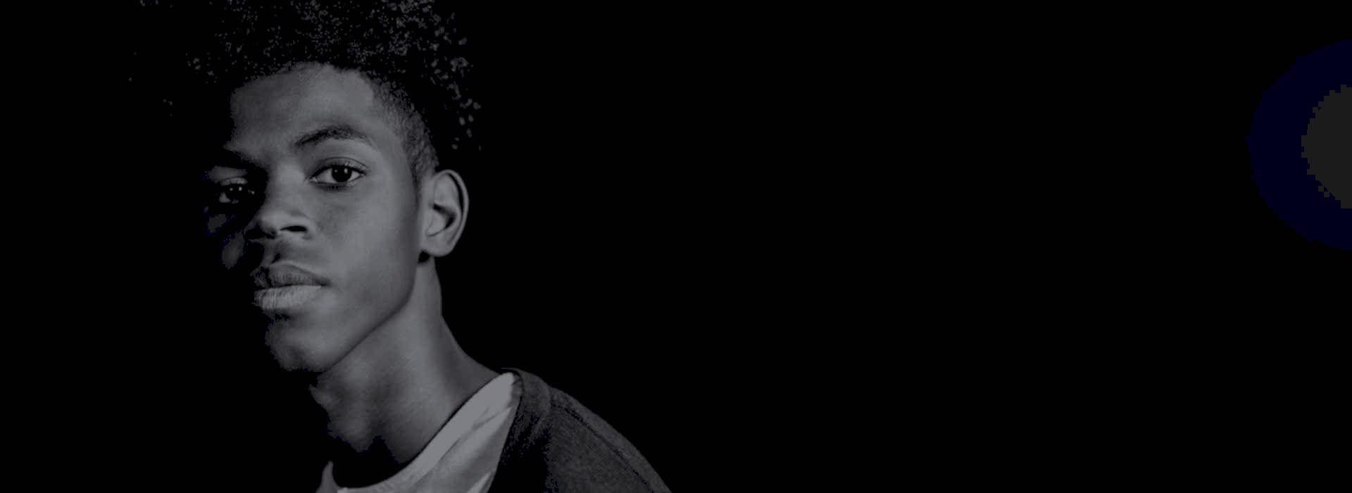 A young man with a strong expression looks out from deep shadow