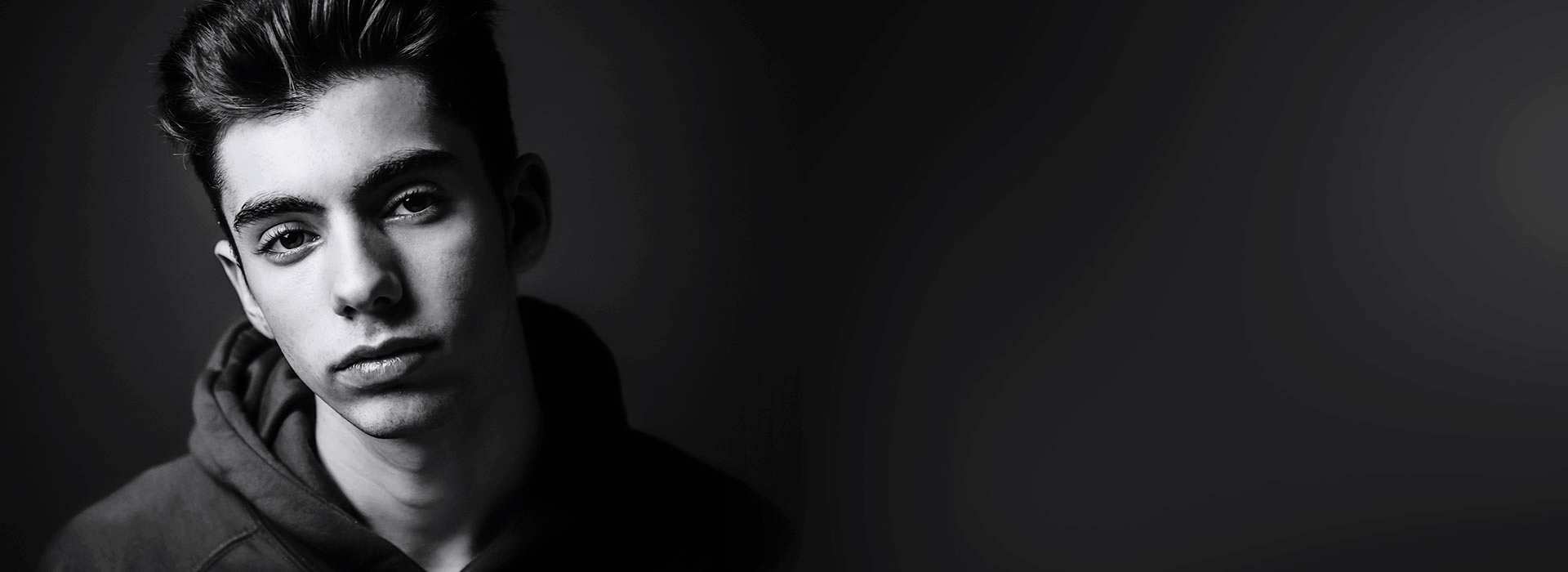 A young man in deep shadow looks at us with expectation