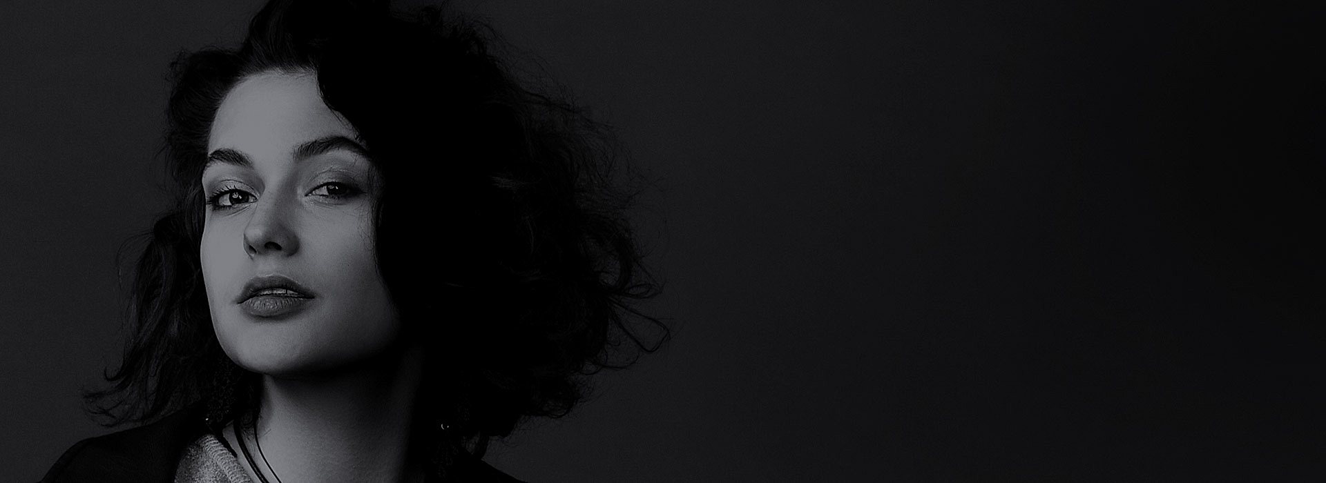 A young woman in deep shadow looks at us with a curious expression