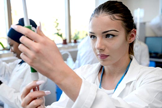 A young woman in a lab coat works with care and concentration in a science lab