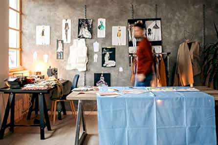 A man crosses to the window of his small fashion studio