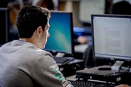 A young man sits at a computer his face in profile highlighted by the sun