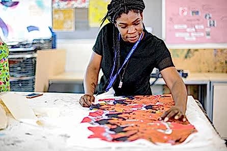 A young woman in a bright textile studio spreads out a beautifully screen-printed African patterned fabric