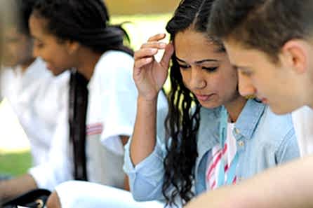 A young woman discussing her assignment with other students sitting outside in the campus grounds