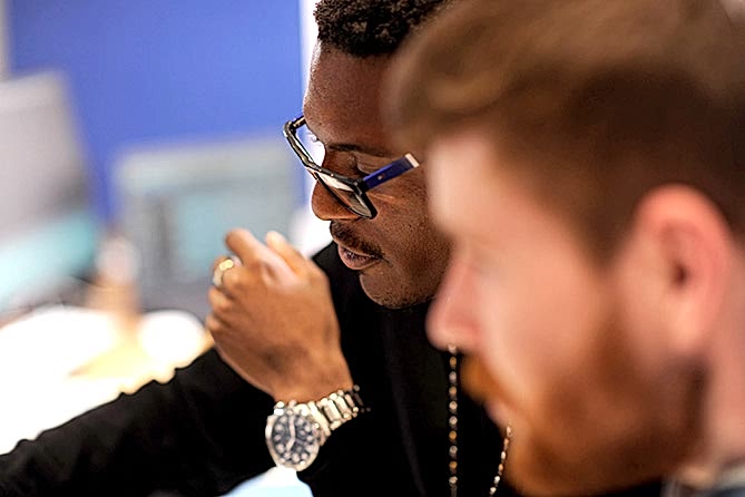 The young man in the foreground is blurred behind him his friend reaches for something off camera