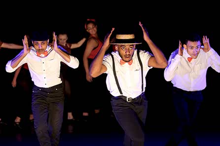 A chorus line of young men in a stage musical rakishly tip their straw boaters